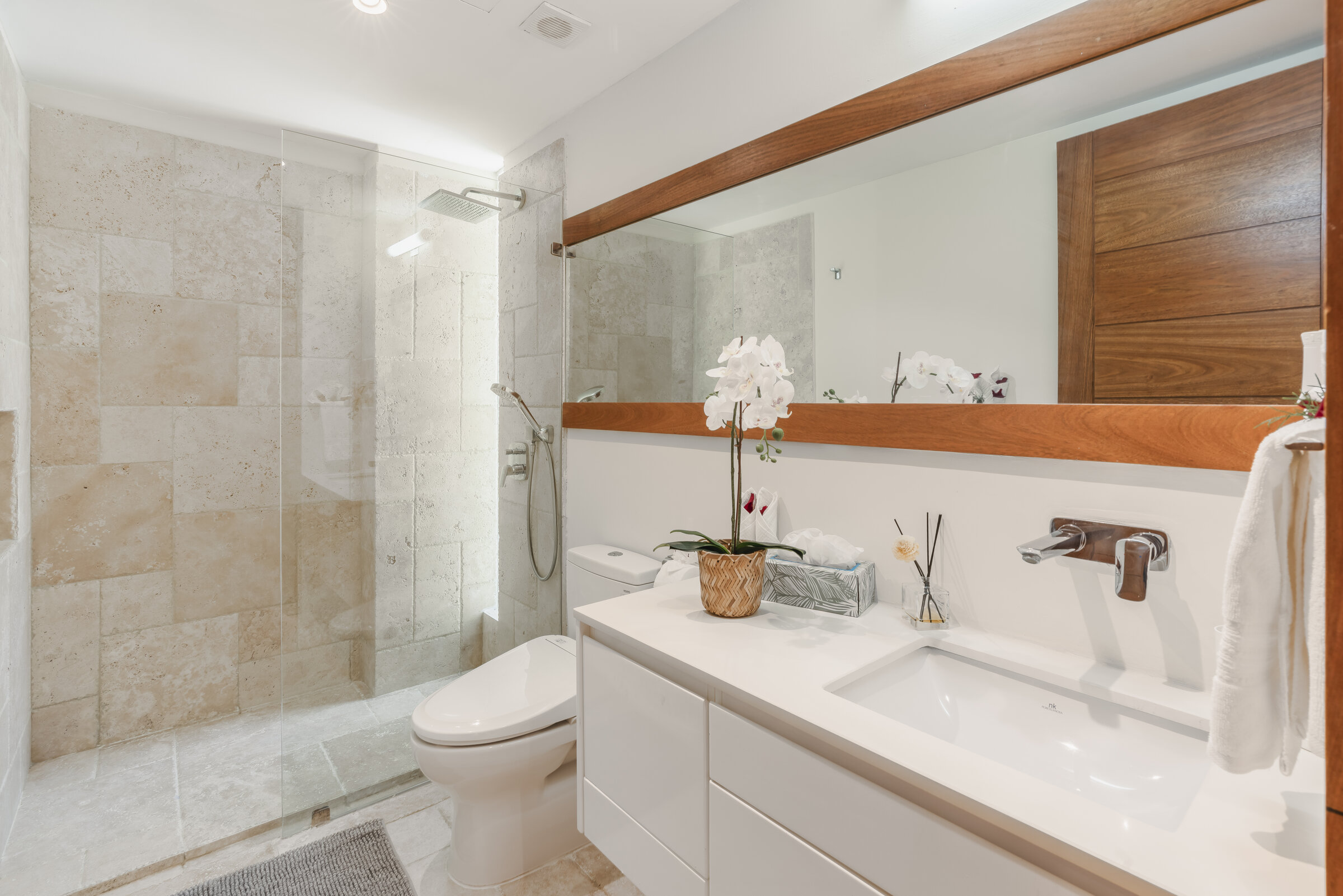 Baño moderno Villa Eden — ducha de piedra travertino y tocador blanco