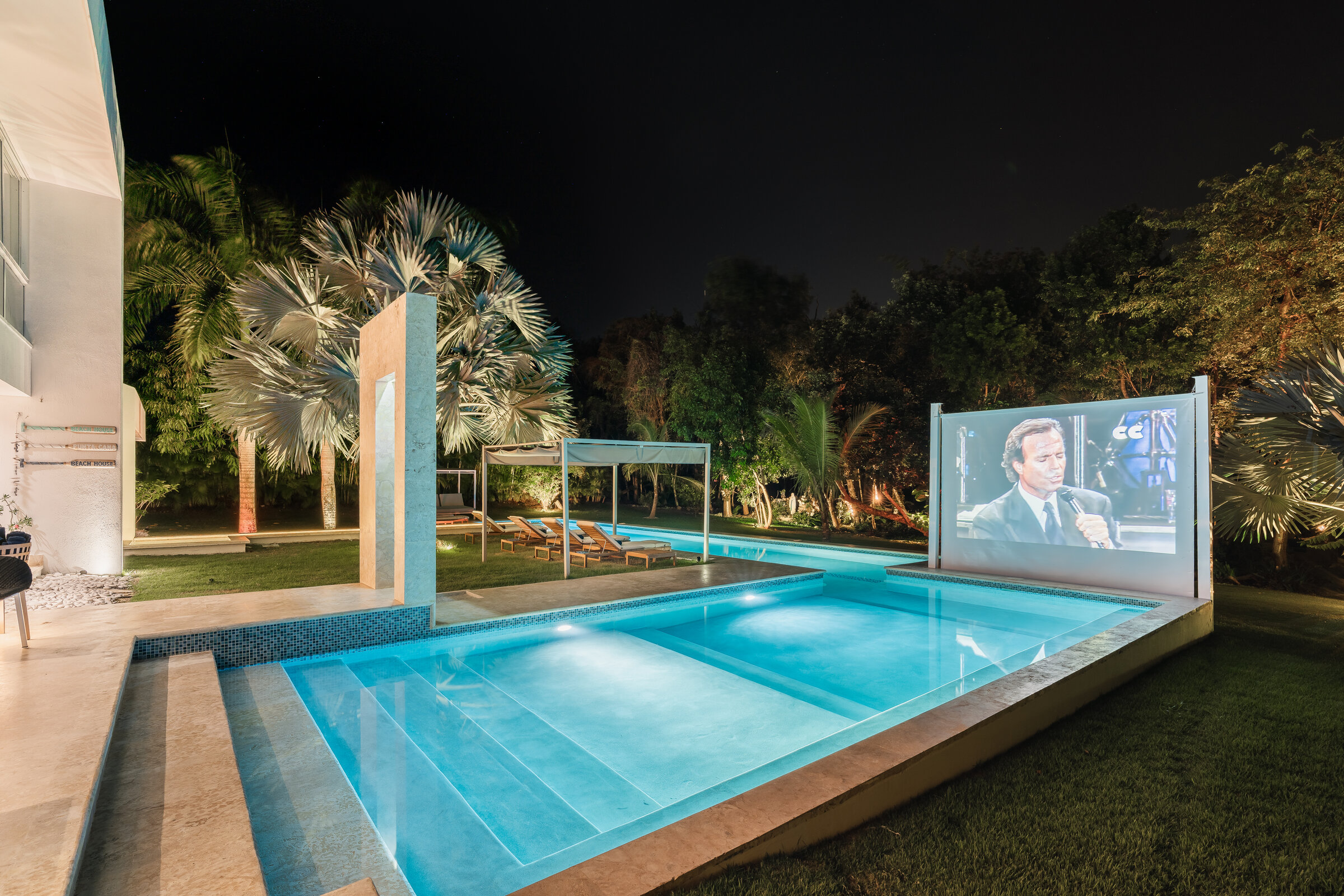 Piscina nocturna Villa Eden — pantalla de cine al aire libre entre palmeras