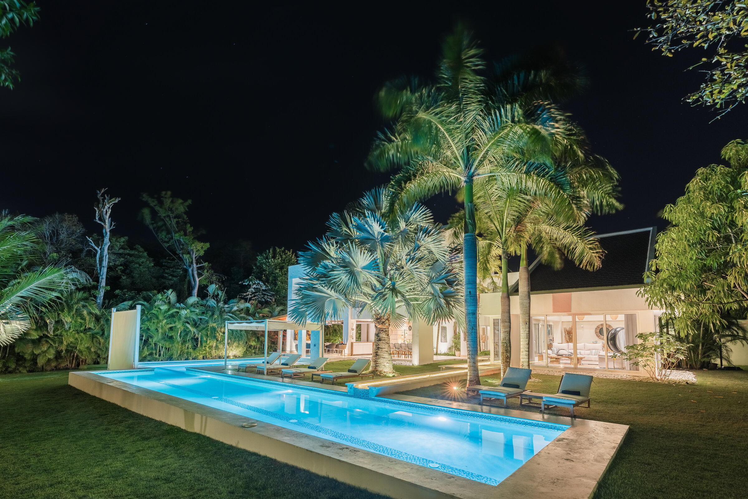 Jardín y piscina Villa Eden de noche — palmeras iluminadas y área lounge